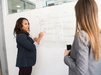 two women conversing in front of a whiteboard