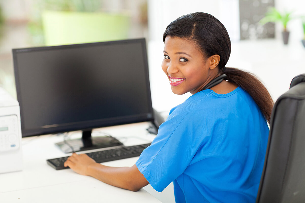 A smiling woman working on medical data entry into a computer.