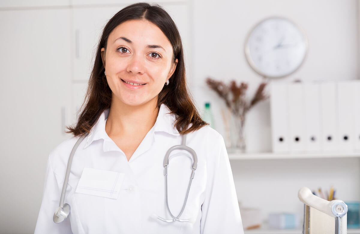 A smiling woman with a stethoscope wearing a lab coat.